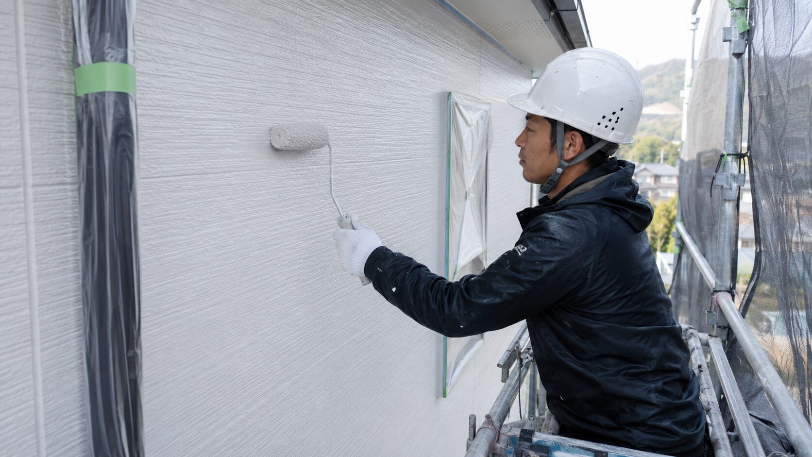 住宅の外壁をローラーで丁寧に塗装する職人