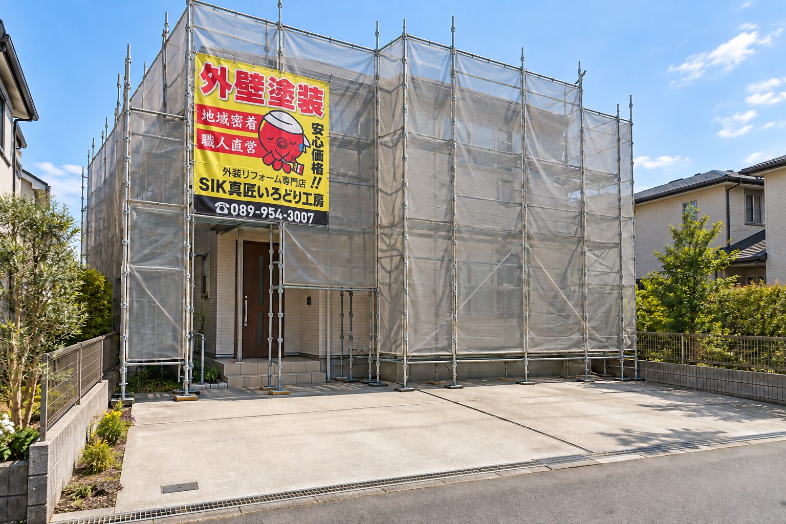 SIK真匠いろどり工房イメージシートを掲げた足場と、住宅前面の駐車スペース